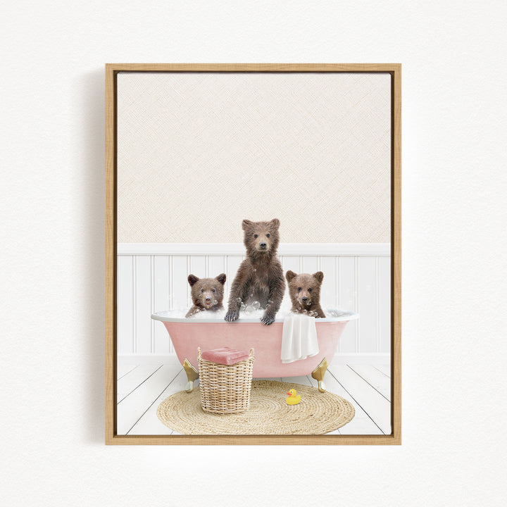 A framed image depicting three brown bears sitting in a pink bathtub, with a basket of toys nearby.