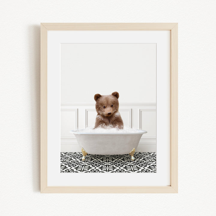 A cute brown bear sitting in a white bathtub filled with bubbles, surrounded by a black and white patterned rug.