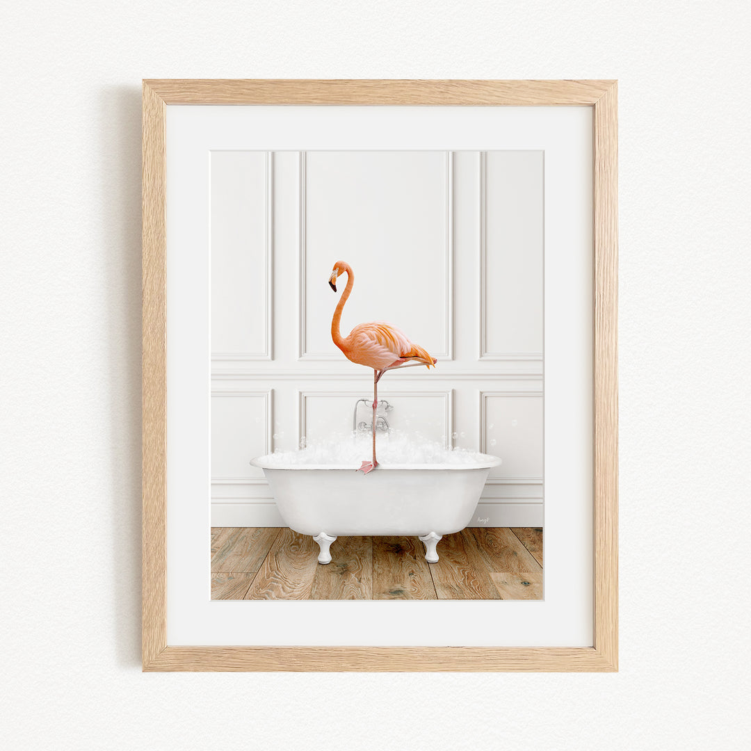 A framed image of a pink flamingo standing on the edge of a white clawfoot bathtub, with a wooden floor and white walls in the background.