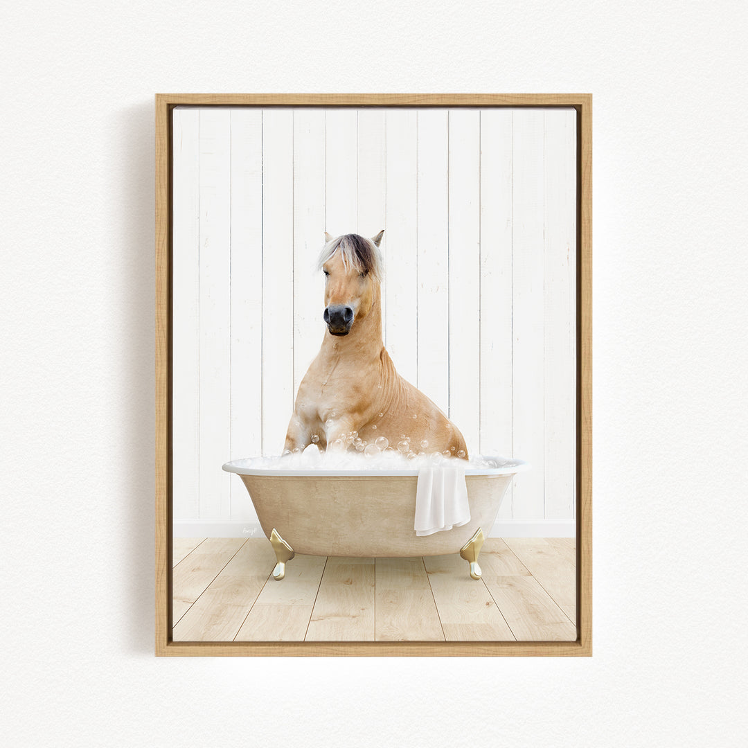 A light brown horse is sitting in a white bathtub filled with bubbles, with a towel hanging on the side of the tub.