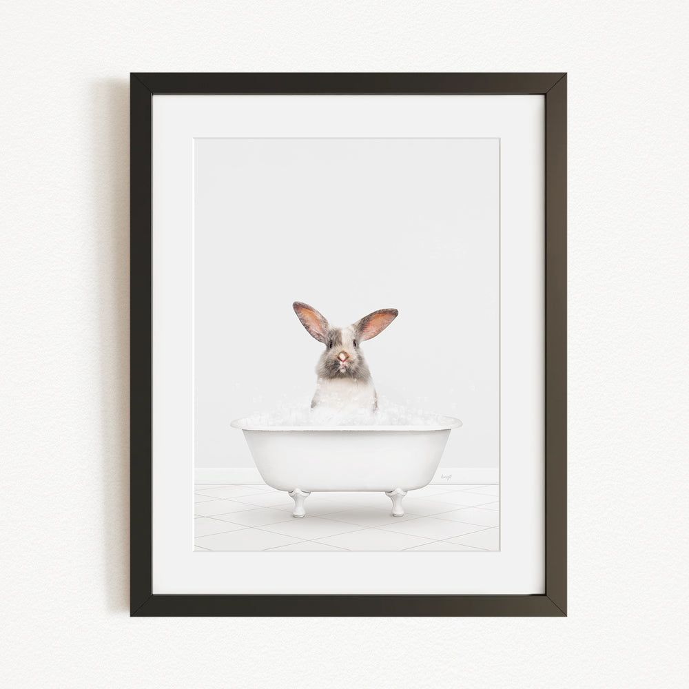 A white rabbit sitting in a white bathtub filled with bubbles, looking directly at the camera.
