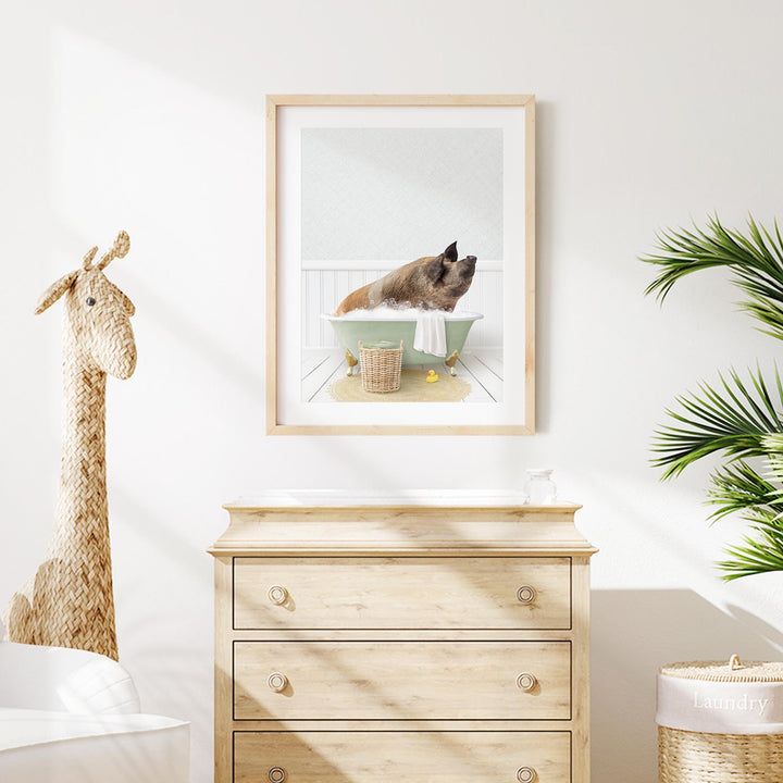 A framed image of a pig bathing in a tub is displayed on a white wall above a wooden dresser.