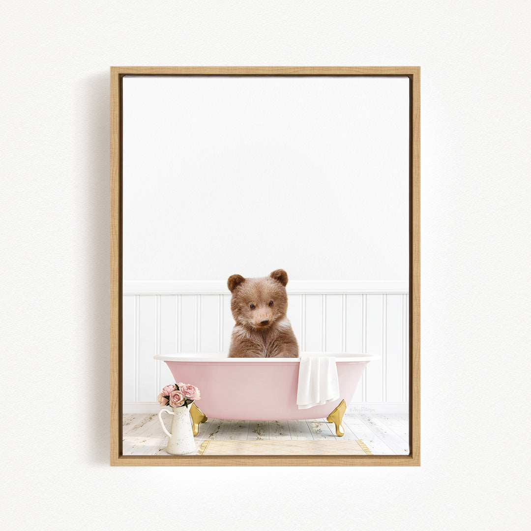 A brown bear sitting in a pink bathtub, surrounded by a white towel and a vase of flowers.