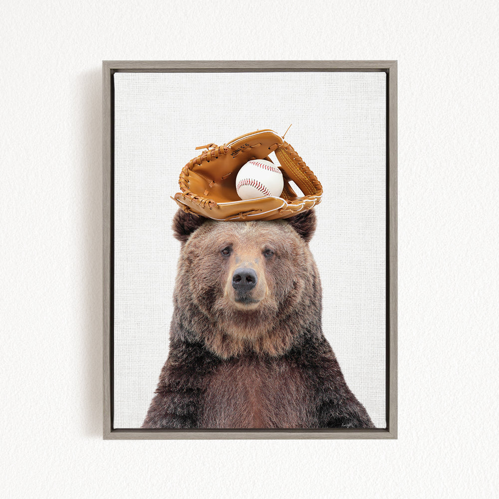 A brown bear wearing a baseball glove on its head, with a baseball resting on top of the glove.