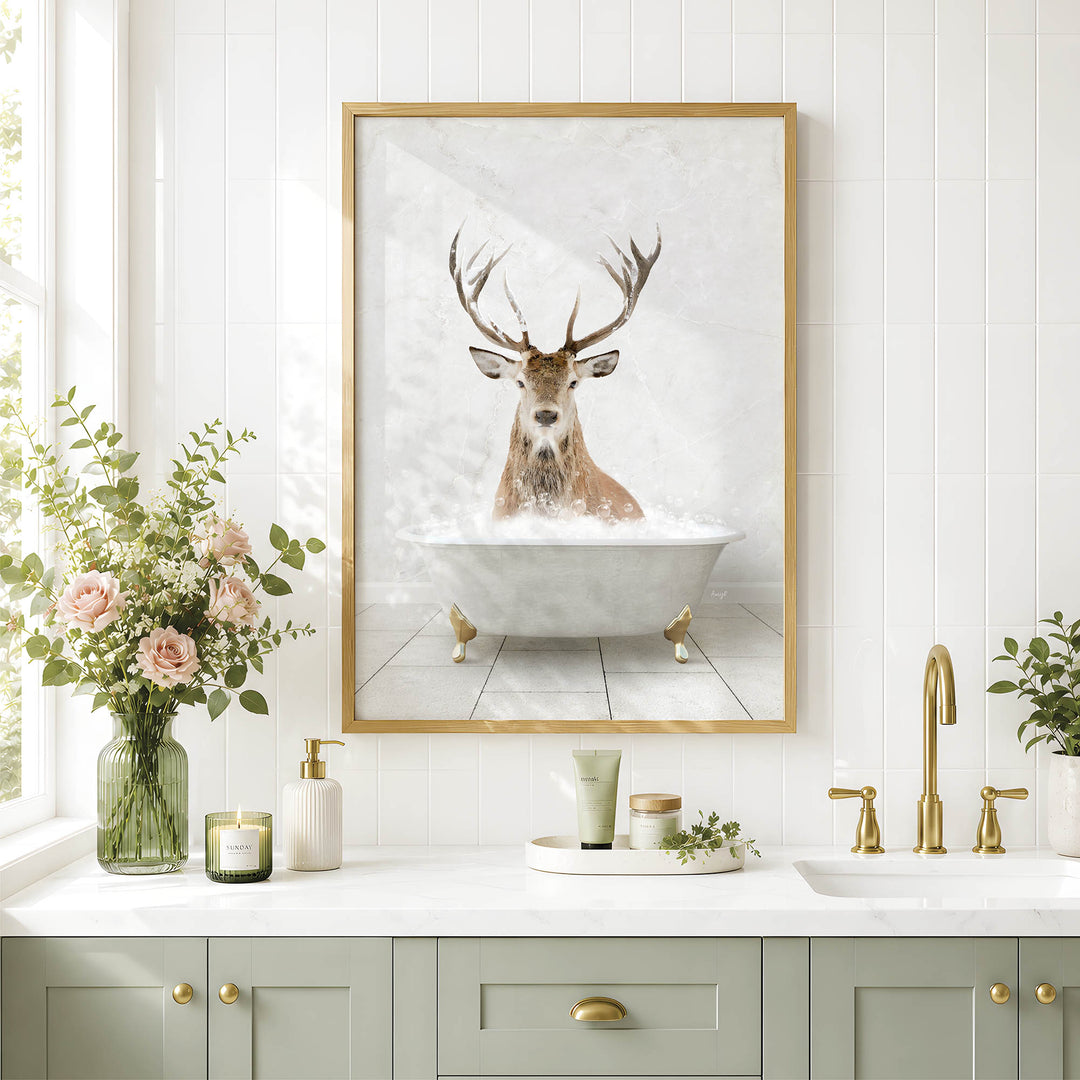 a bathroom with a framed picture of a deer in a bathtub, surrounded by flowers and candles, and a white sink with gold fixtures.