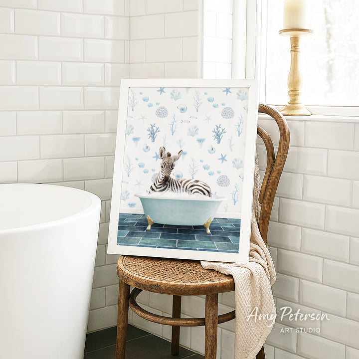 A framed painting of a zebra sitting in a bathtub is displayed on a wooden chair in a bathroom setting.