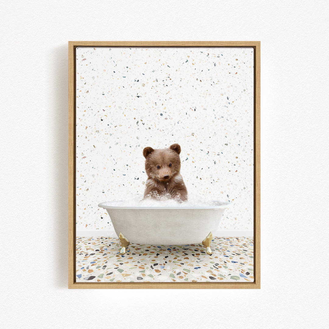 A cute brown bear sitting in a white bathtub filled with water, surrounded by a speckled tiled floor.