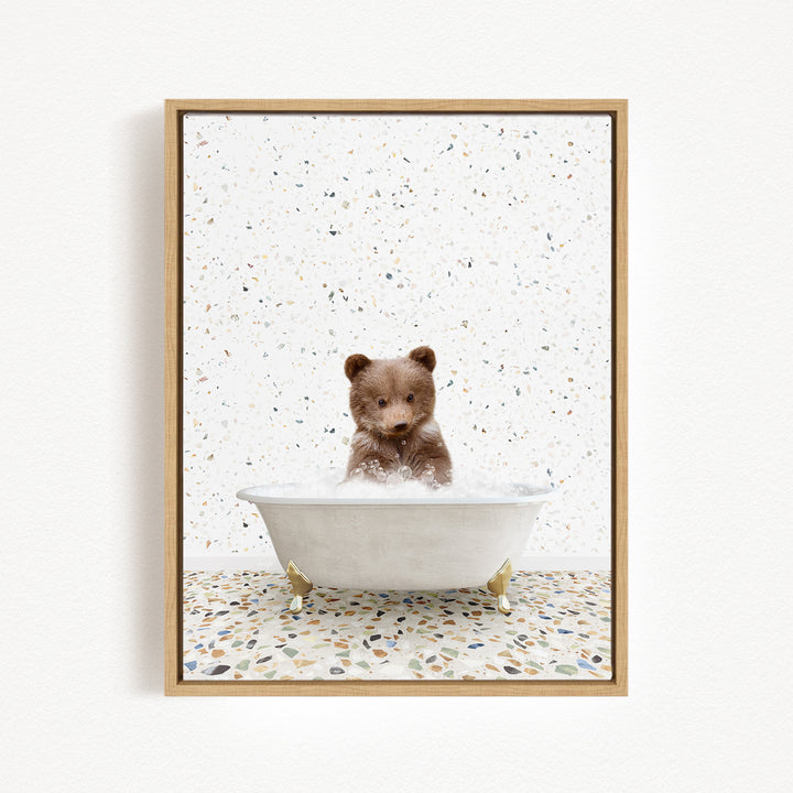 A cute brown bear sitting in a white bathtub filled with water, surrounded by a speckled tiled floor.