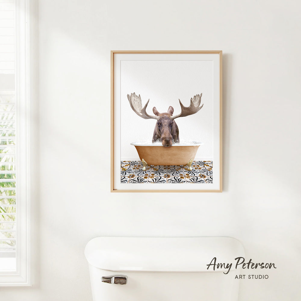 A framed image of a moose sitting in a bathtub, with its antlers raised, is hanging on a white wall.