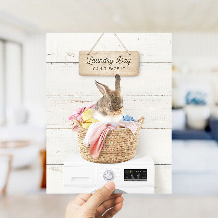A hand holding a laundry basket containing a rabbit, with a sign above that says "Laundry Day Can't Face It".