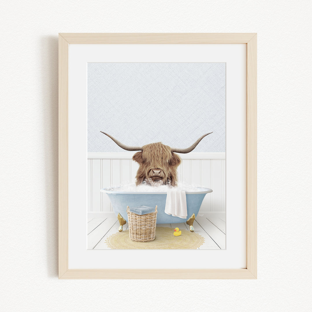 A framed image depicting a Highland cow with large horns sitting in a bathtub filled with water and surrounded by various objects, including a yellow rubber duck.