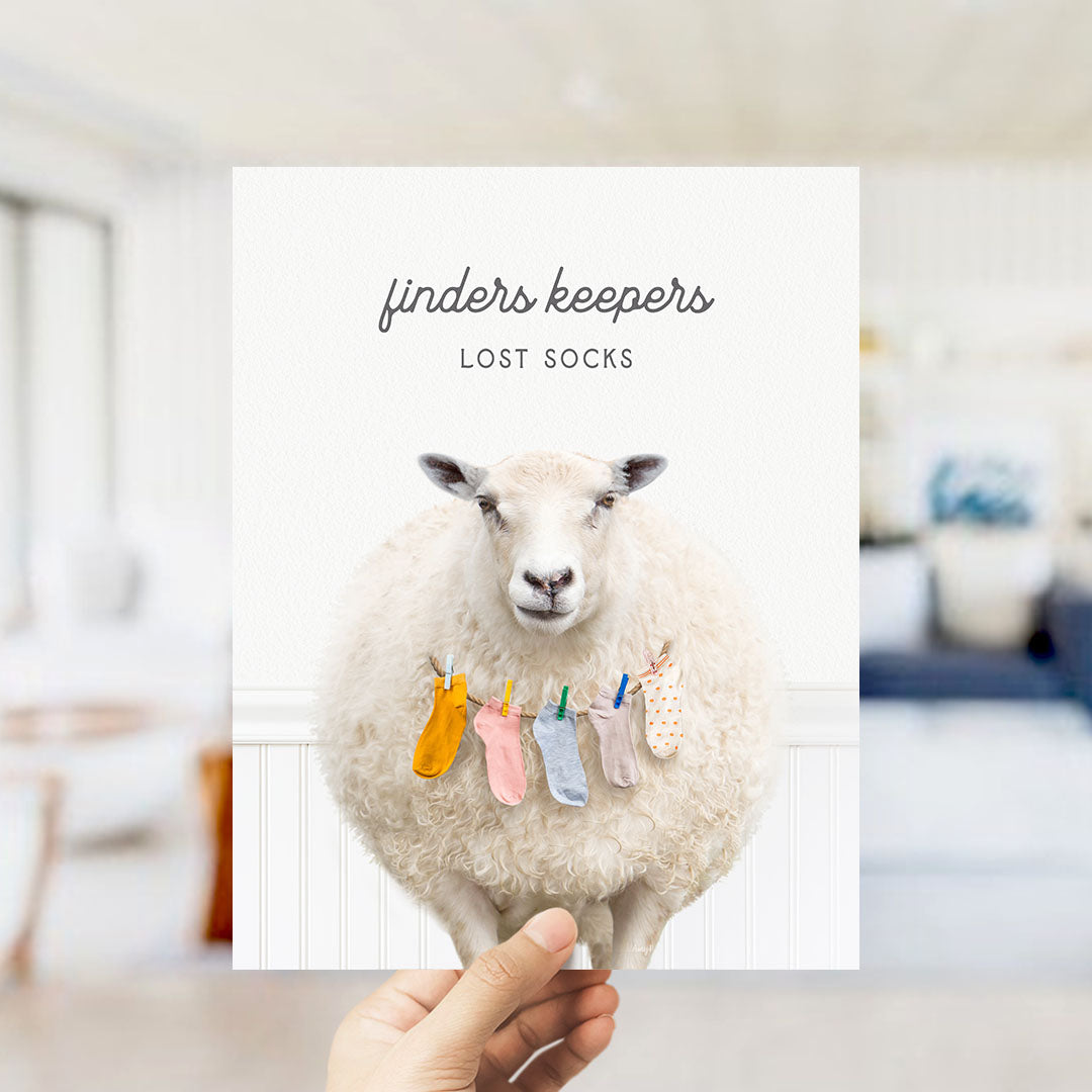 A hand holding a white sheep with colorful socks hanging from its neck, against a white background.