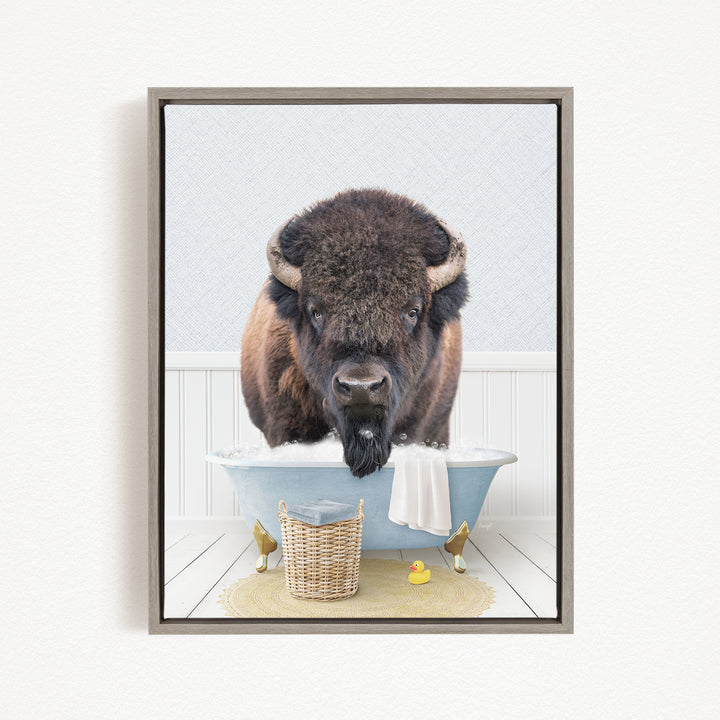 A buffalo with a long, shaggy mane is sitting in a blue bathtub, surrounded by a yellow rubber duck and a wicker basket.