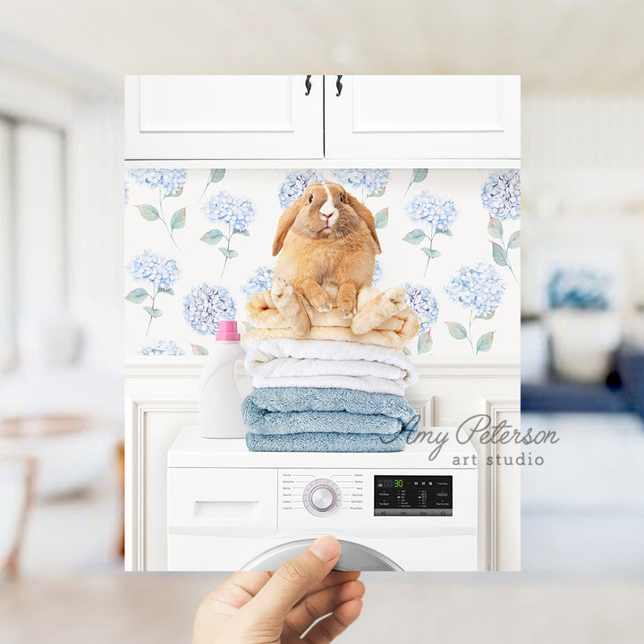 a person holding up a picture of a rabbit on top of a stack of towels