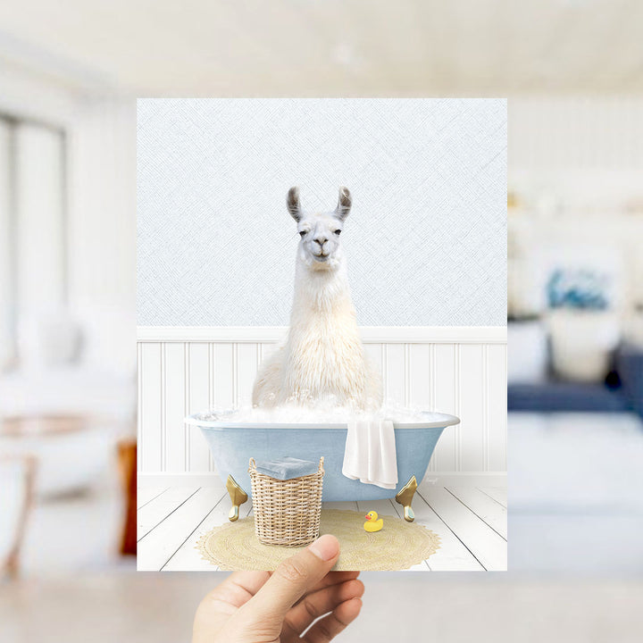 A white llama sitting in a blue bathtub filled with bubbles, with a yellow rubber duck nearby.