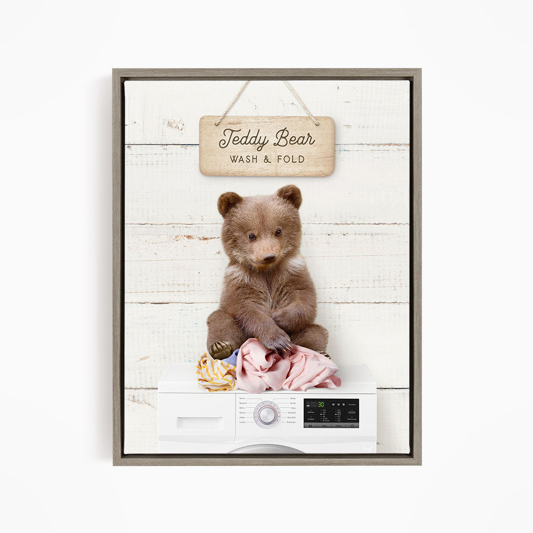 A teddy bear sitting on a pile of laundry, with a sign above that says "Teddy Bear Wash & Fold".