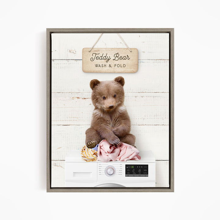 A teddy bear sitting on a pile of laundry, with a sign above that says "Teddy Bear Wash & Fold".
