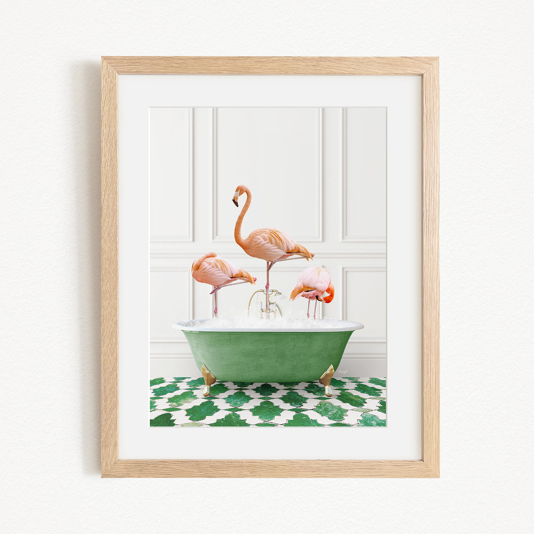 A framed image depicting three flamingos standing in a green bathtub filled with water, set against a white wall with a green and white patterned floor.