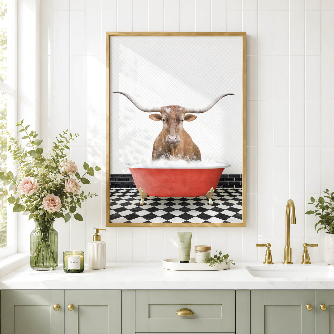 a framed picture of a bull with long horns sitting in a red bathtub, surrounded by a black and white checkered floor and a white countertop with various bathroom accessories.