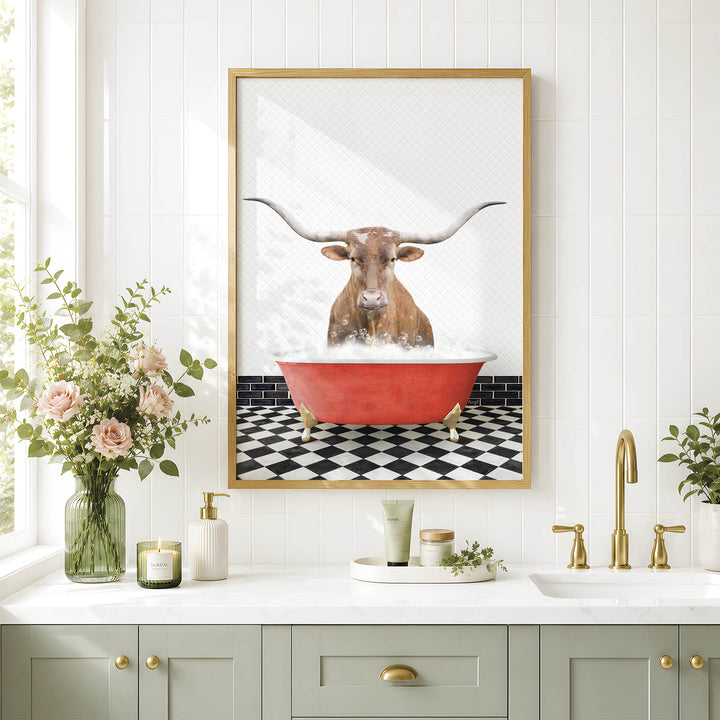 a framed picture of a bull with long horns sitting in a red bathtub, surrounded by a black and white checkered floor and a white countertop with various bathroom accessories.