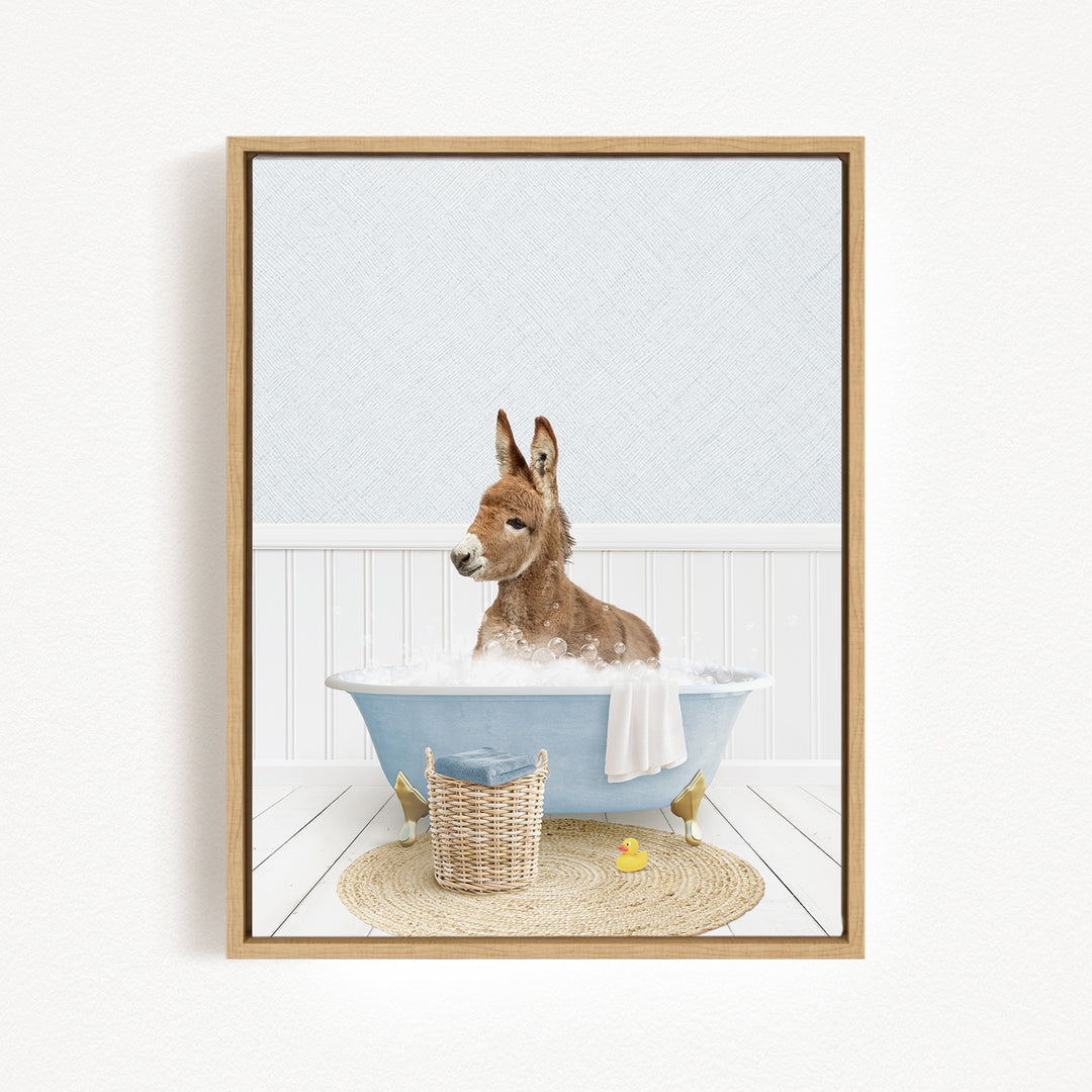 A donkey is sitting in a blue bathtub filled with water, surrounded by a basket, a yellow rubber duck, and a white towel.