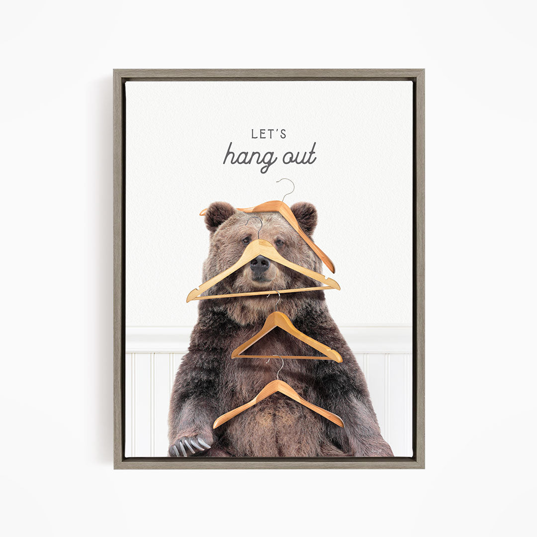A large brown bear sitting on a white wall, surrounded by hanging wooden hangers.