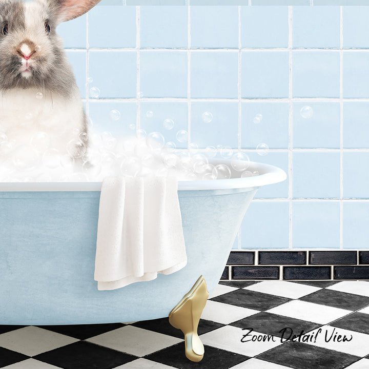 A fluffy gray rabbit sitting in a blue bathtub filled with bubbles, with a towel and gold bathtub stopper visible.