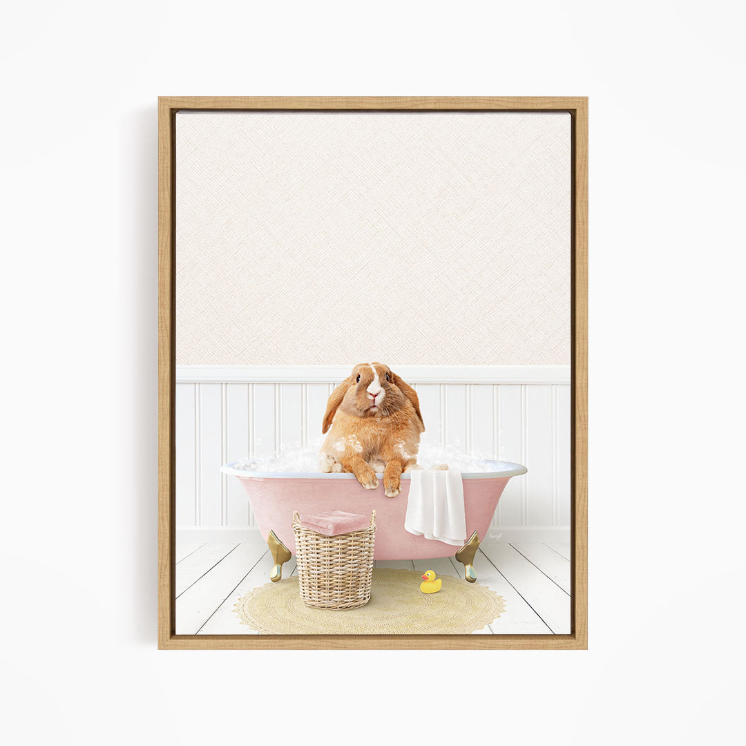 A brown rabbit sitting in a pink bathtub filled with bubbles, surrounded by a yellow rubber duck and a white towel.