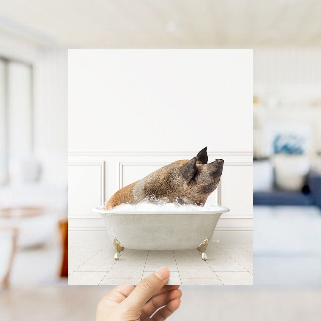 A hand holds up a framed image of a pig sitting in a bathtub filled with bubbles.