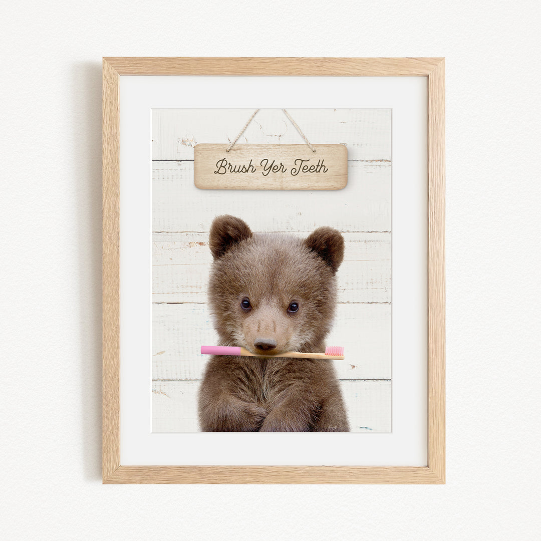 A cute brown bear holding a pink toothbrush in front of a wooden sign that says "Brush Your Teeth".