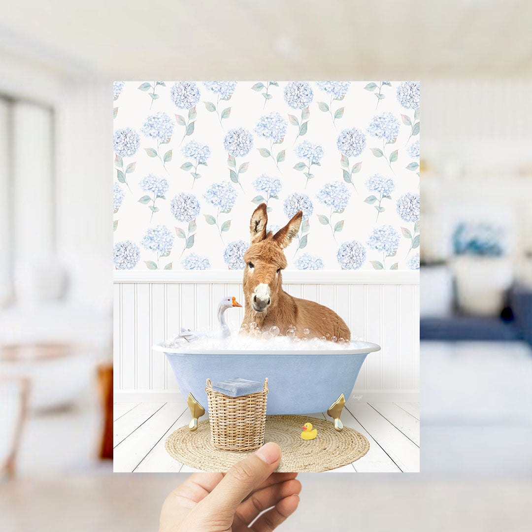 A donkey is sitting in a blue bathtub filled with bubbles, surrounded by a wicker basket and a rubber duck.