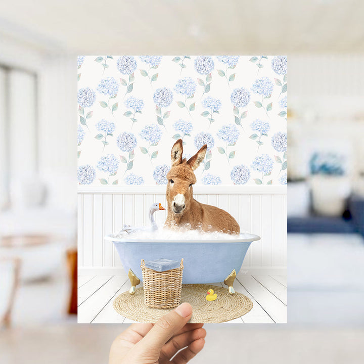 A donkey is sitting in a blue bathtub filled with bubbles, surrounded by a wicker basket and a rubber duck.