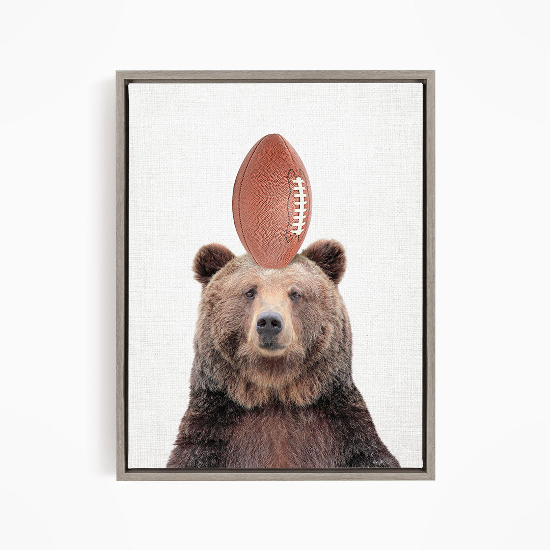 A brown bear standing on its head with a football on top of its head.