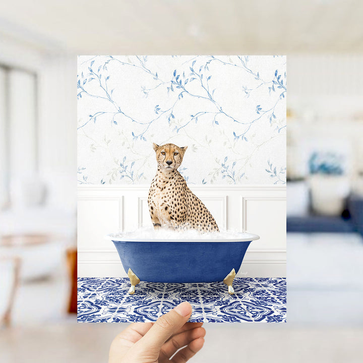 A cheetah sitting in a blue bathtub filled with water, with a patterned tile floor and a floral wallpaper in the background.