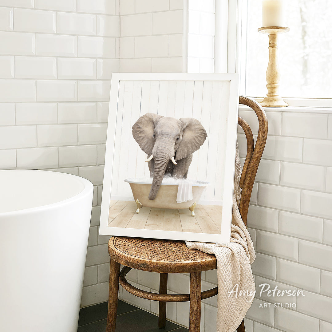 A framed image of an elephant sitting in a bathtub, with a towel draped over the side of the tub.