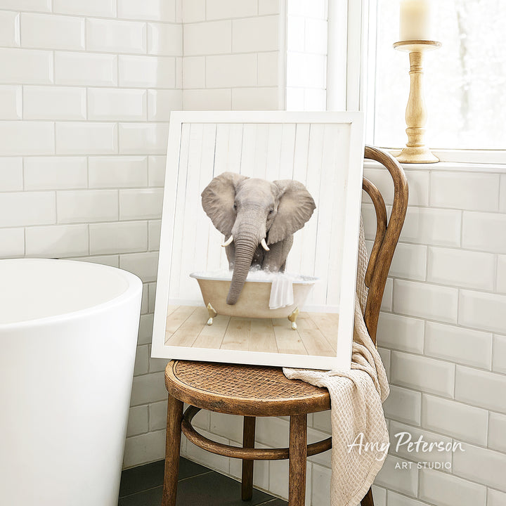 A framed image of an elephant sitting in a bathtub, with a towel draped over the side of the tub.