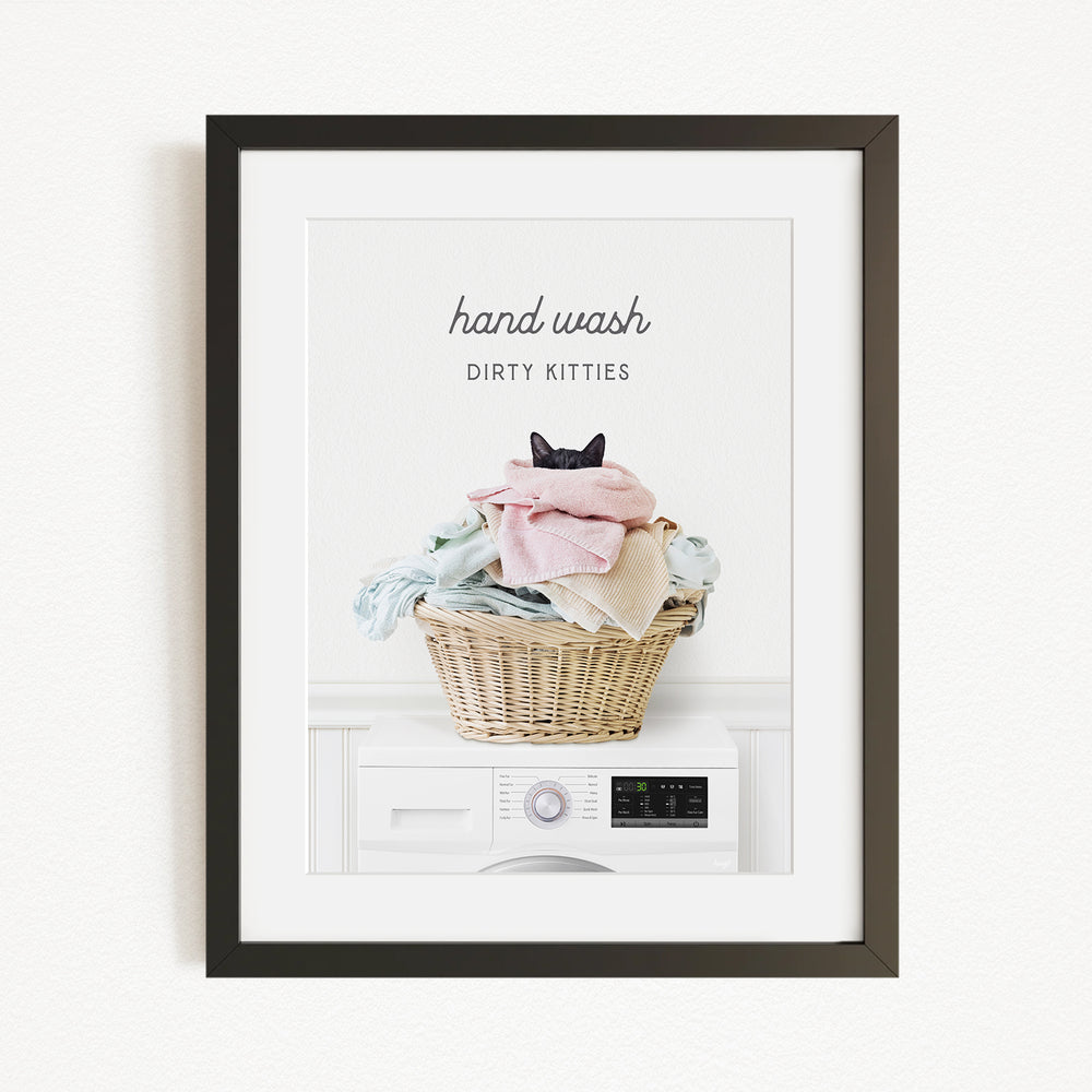 A framed image depicting a cat sitting in a basket filled with laundry, with the text "hand wash dirty kittens" written above the basket.