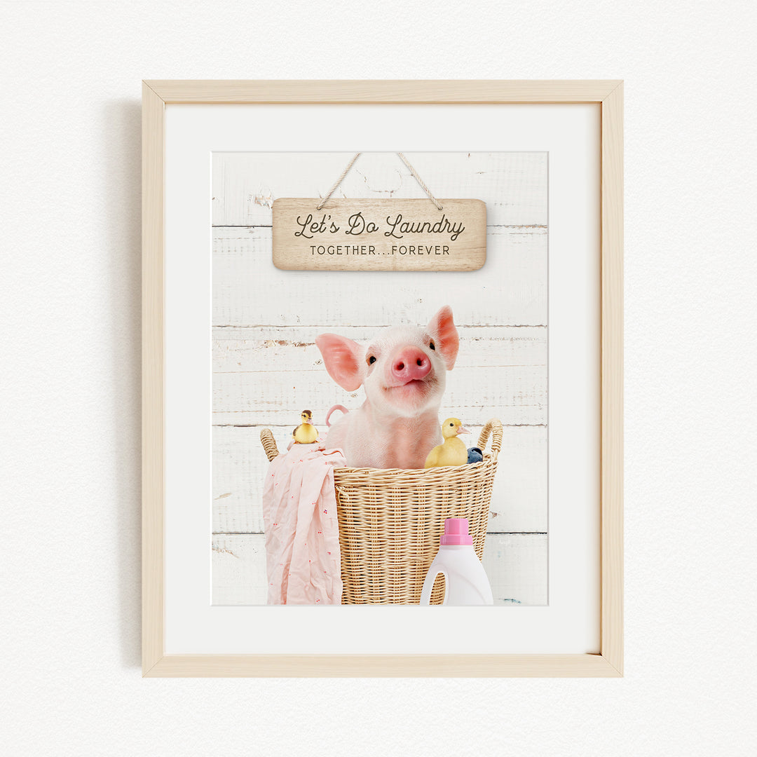 A framed image of a pig sitting in a wicker basket filled with rubber ducks, with a sign above that says "Let's Do Laundry Together Forever".