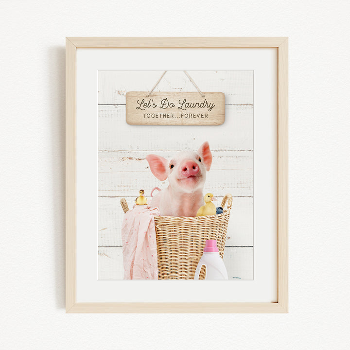 A framed image of a pig sitting in a wicker basket filled with rubber ducks, with a sign above that says "Let's Do Laundry Together Forever".