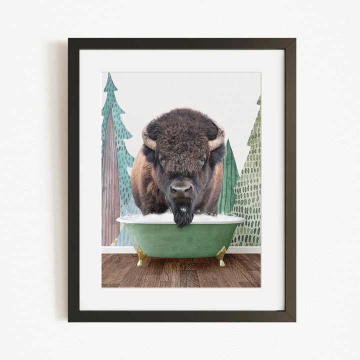 A bison is sitting in a green bathtub, surrounded by pine trees and a snowy landscape.