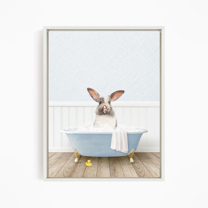 A white rabbit sitting in a blue bathtub filled with bubbles, with a yellow rubber duck nearby.