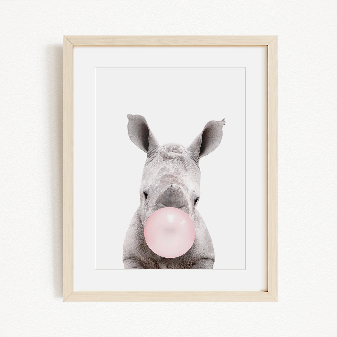 A framed image of a rhinoceros blowing a bubble with a pink bubble gum bubble.