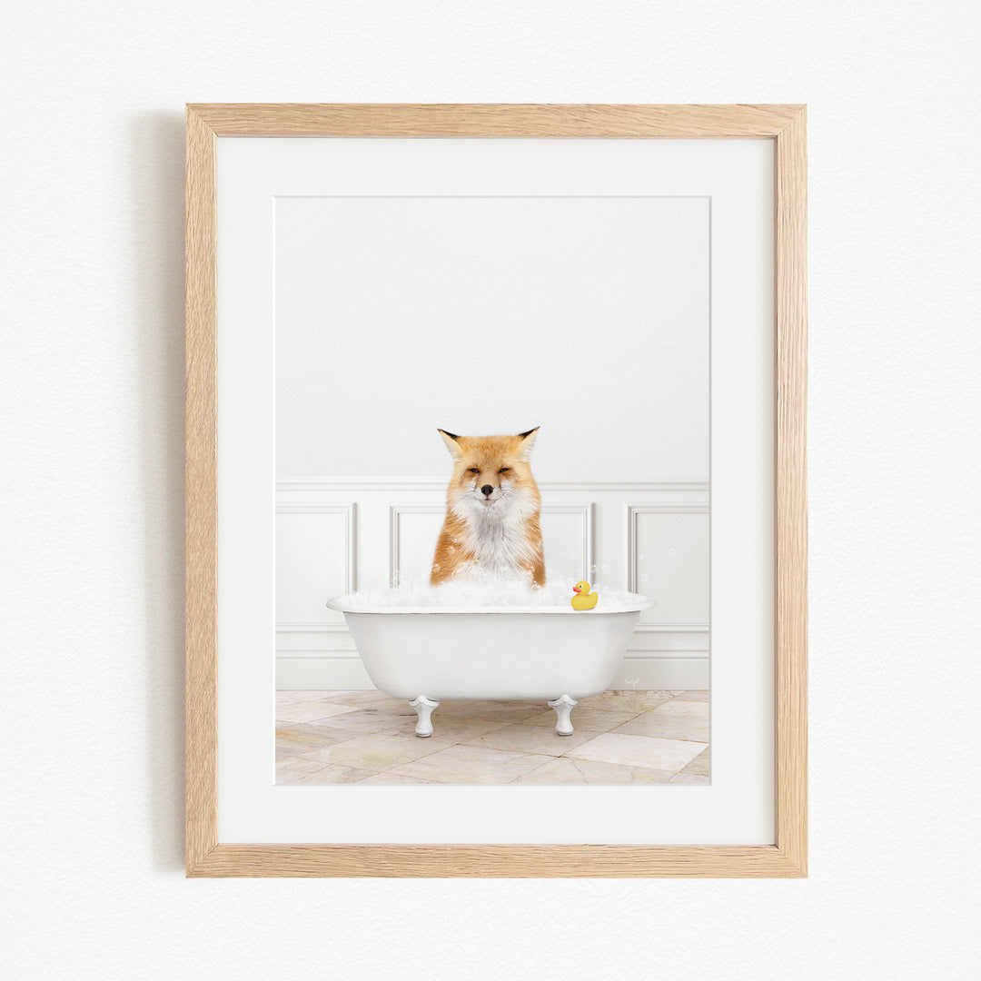 A red fox is sitting in a white bathtub filled with bubbles, with a yellow rubber duck floating in the water.