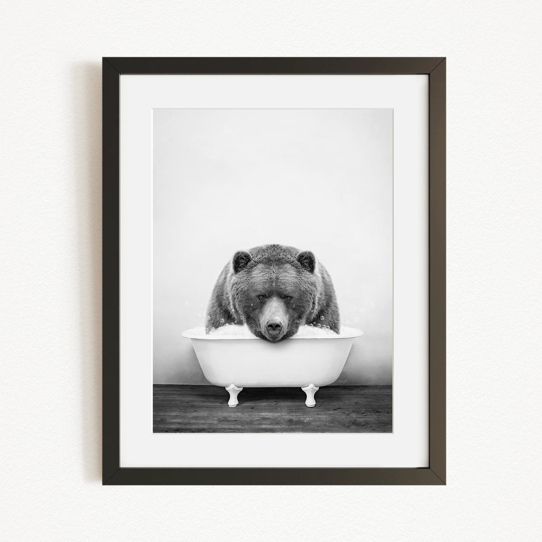 A black and white photograph of a bear sitting in a bathtub filled with water.