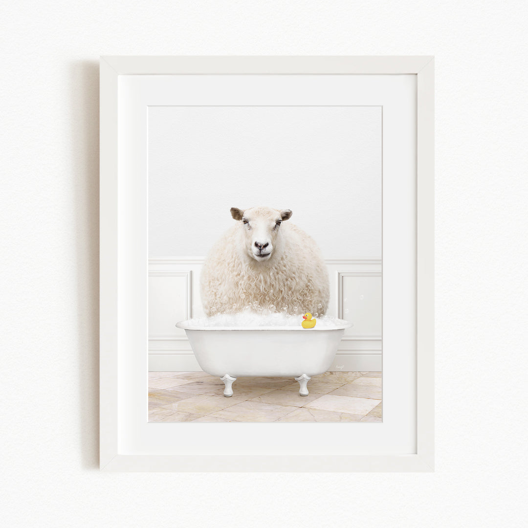 A fluffy white sheep sits in a white bathtub filled with bubbles, with a yellow rubber duck floating in the water.