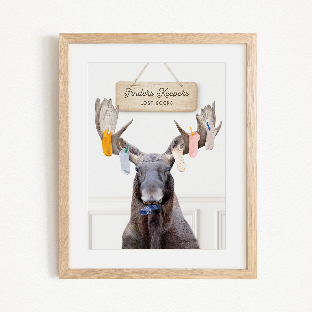A framed image of a moose with a sign that says "Finders Keepers" hanging above it, along with several socks hanging from its antlers.