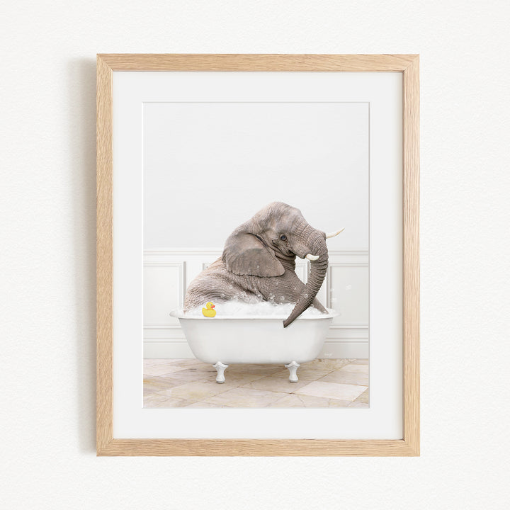 A gray elephant is sitting in a white bathtub, with a yellow rubber duck floating in the water.