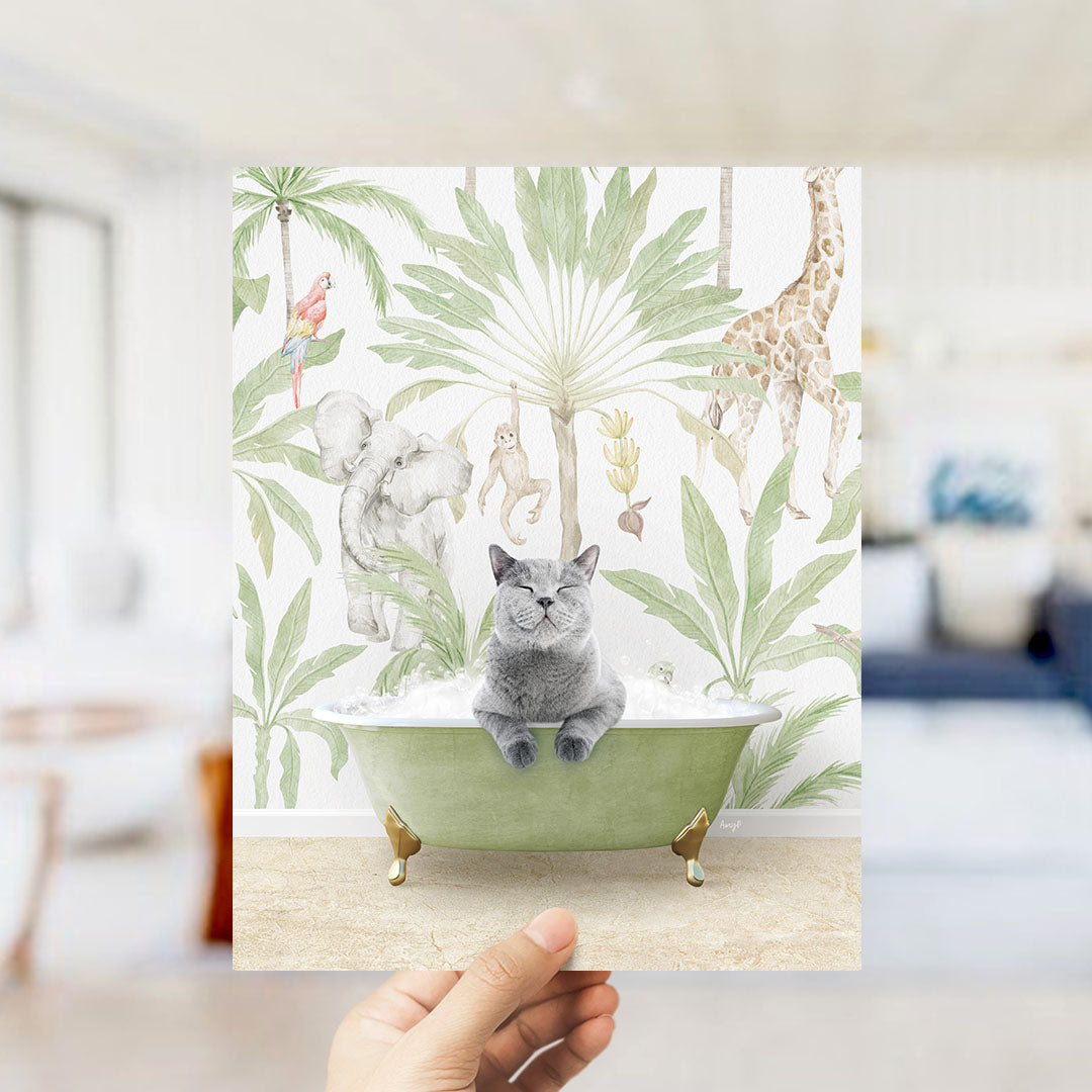 A hand holds up a framed print featuring a whimsical scene of a cat sitting in a bathtub surrounded by tropical plants and animals, including a giraffe and a parrot.