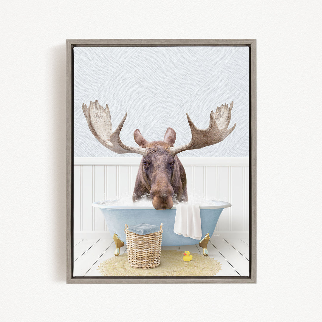 A moose with large antlers is sitting in a bathtub filled with water, surrounded by a yellow rubber duck and a wicker basket.