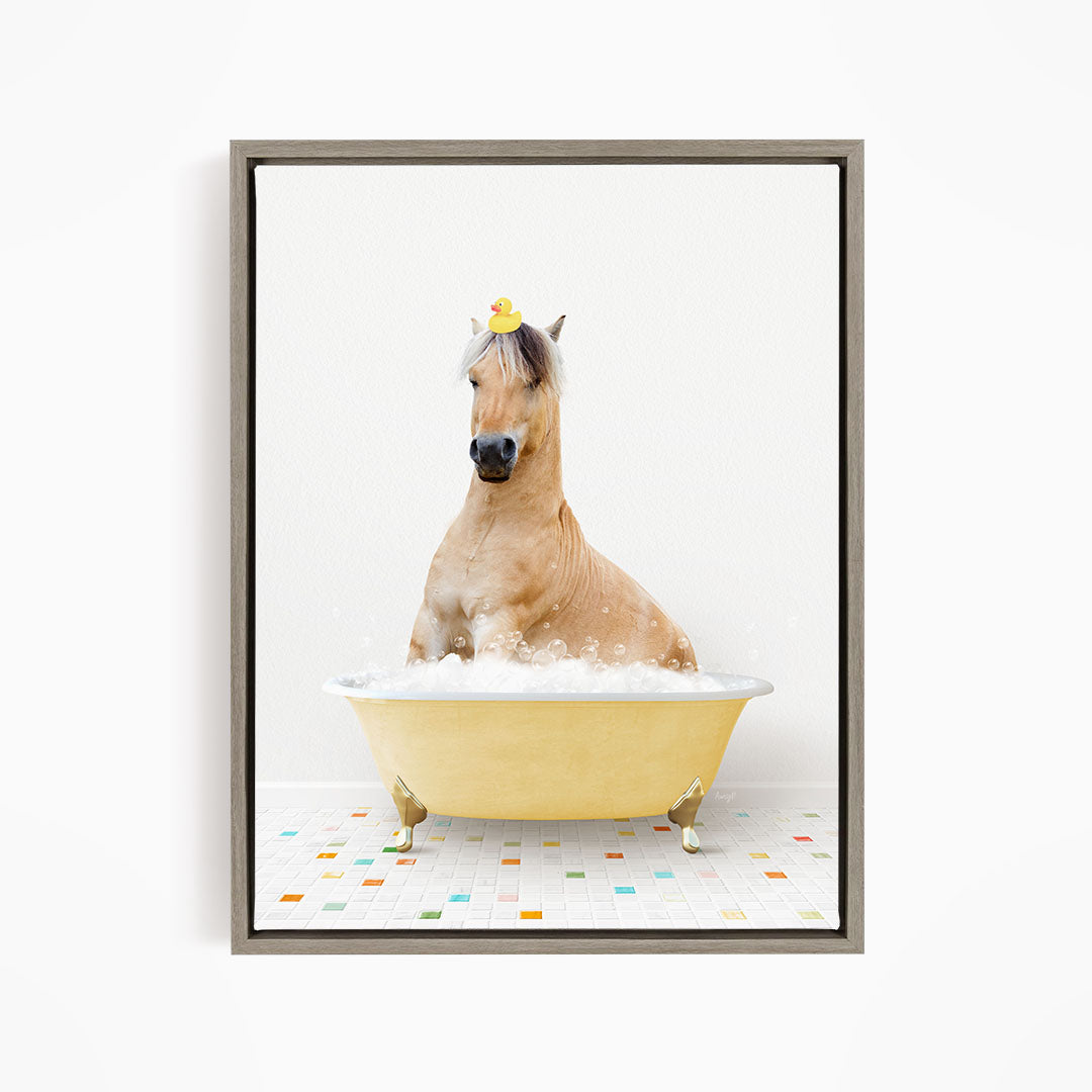 A light brown horse is sitting in a yellow bathtub filled with bubbles, wearing a yellow rubber duck on its head.
